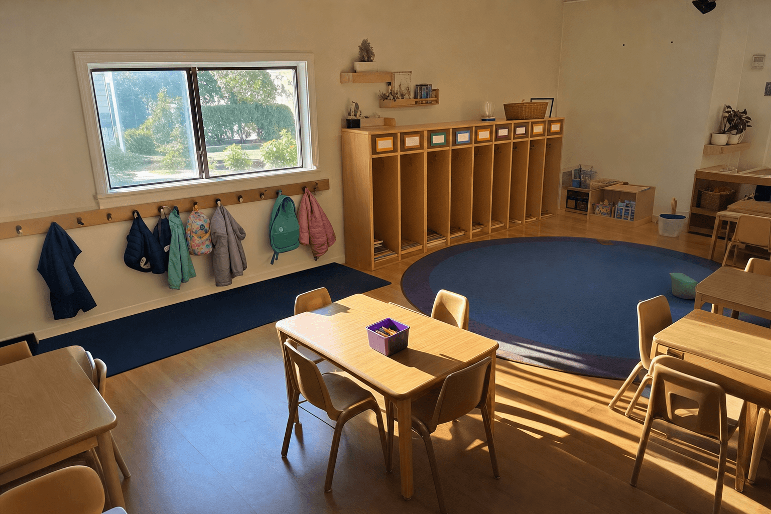 A snapshot of an empty preschool classroom with a low window beside the coat hooks